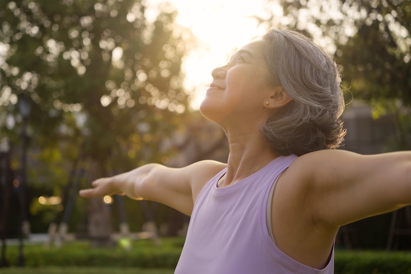 older-woman-stretching-her-arms-outdoors-at-sunrise